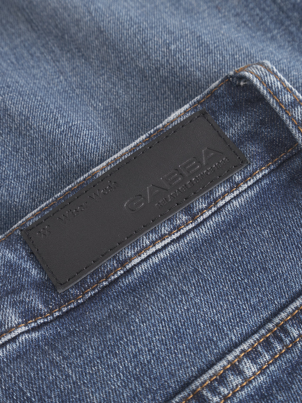 Close-up of GABmarc F1010 dark blue denim jeans with a black leather Gabba patch and text above it, stitched on the waistband near the back pocket.