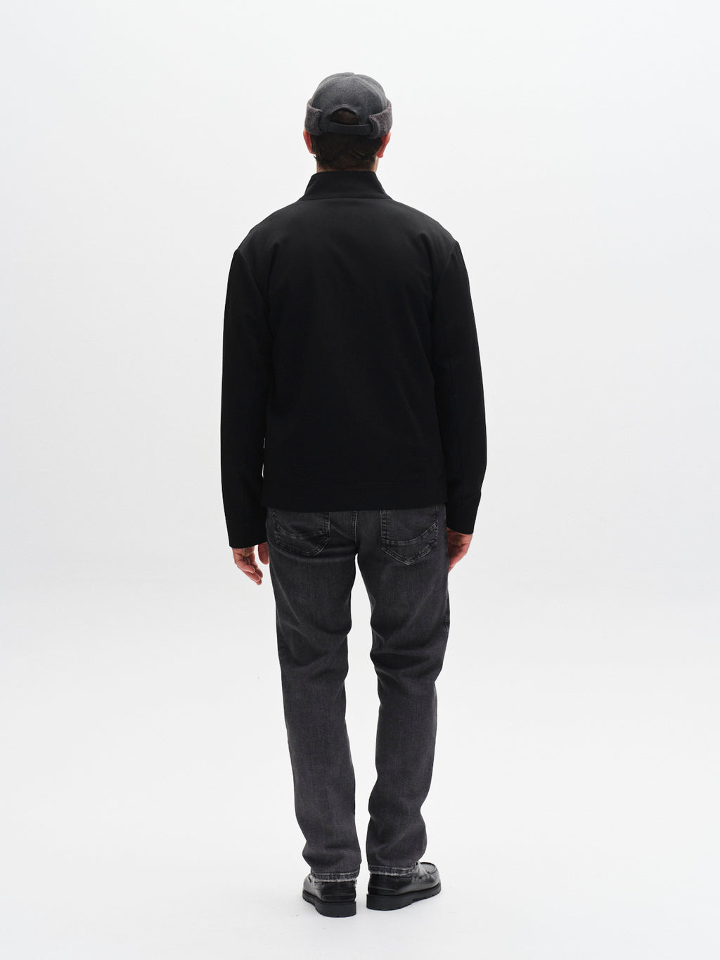 A person wearing Gabba's GABmarc F1011 - Black Denim jeans, a black jacket, black shoes, and a gray cap stands with their back to the camera against a plain white background.