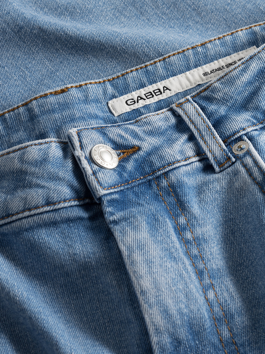 Close-up of Marc F1012 - Lt. Blue Denim jeans by Gabba, showing a silver button, belt loops, and a white GABBA label on the waistband. These regular fit jeans feature visible texture and stitching for a modern classic look.