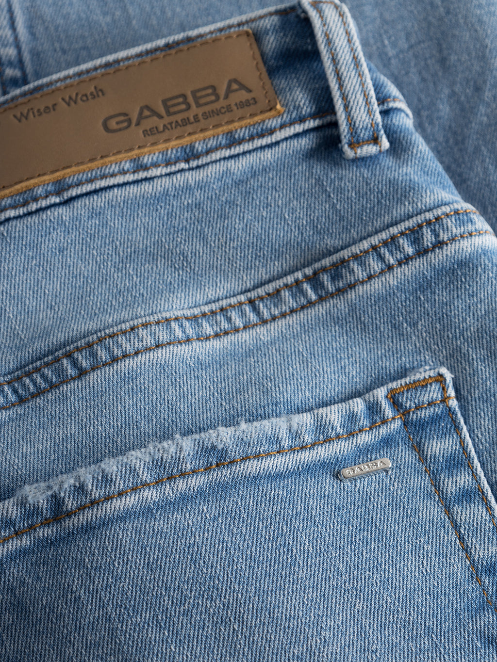 Close-up of Gabba Marc F1012 light blue denim jeans shows a brown leather brand patch, metallic front pocket tag, visible stitching details, and Wiser Wash technique for a modern classic look.