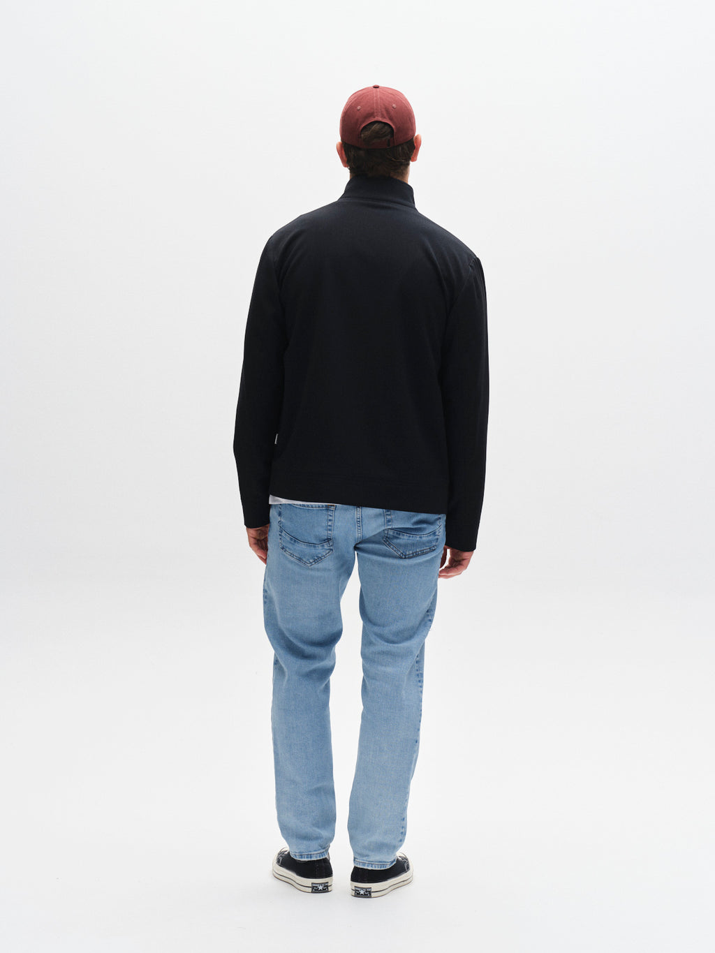 A person stands with their back to the camera wearing a red baseball cap, black jacket, Gabba GABmarc F1012 - Lt. Blue Denim jeans, and black-and-white sneakers against a plain white background.