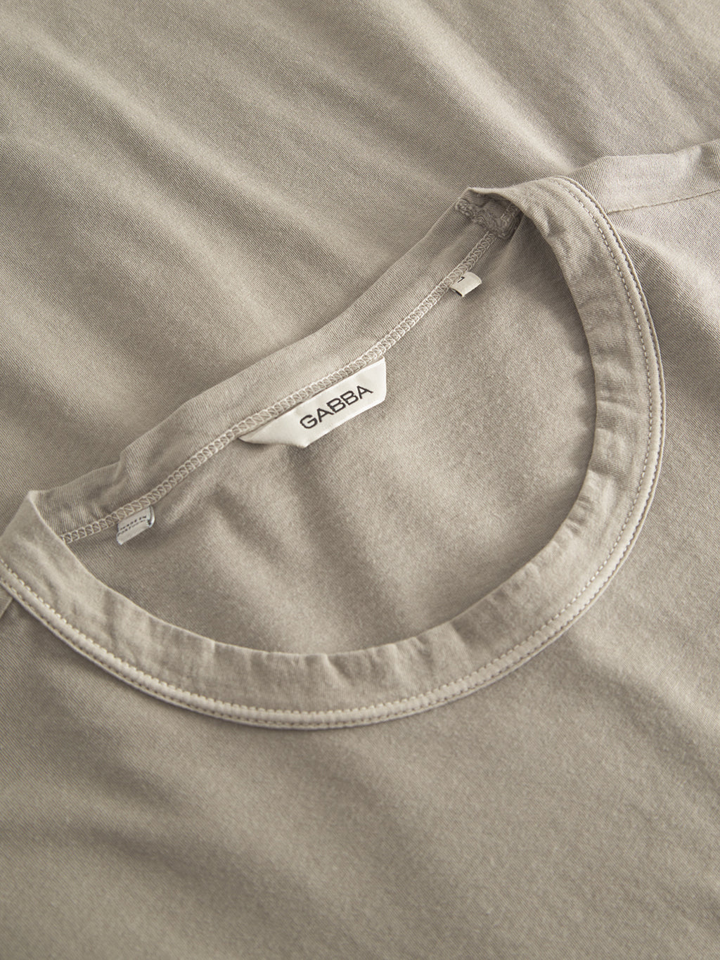 Close-up of a Grey Paloma Lagos SS t-shirt by Gabba laying flat, featuring the collar and inner neck with a visible white Gabba label. Its soft fabric and classic fit make it a versatile piece for any modern wardrobe.