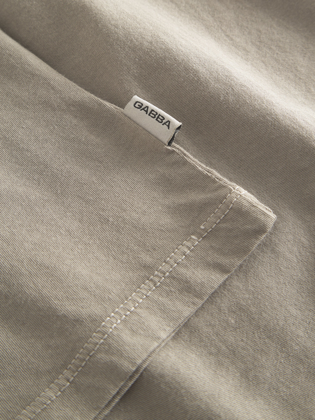 Close-up of the grey Lagos SS by Gabba, featuring visible stitching and a small white Gabba tag near the seam. The contemporary texture and detailing make it a versatile piece for any wardrobe.