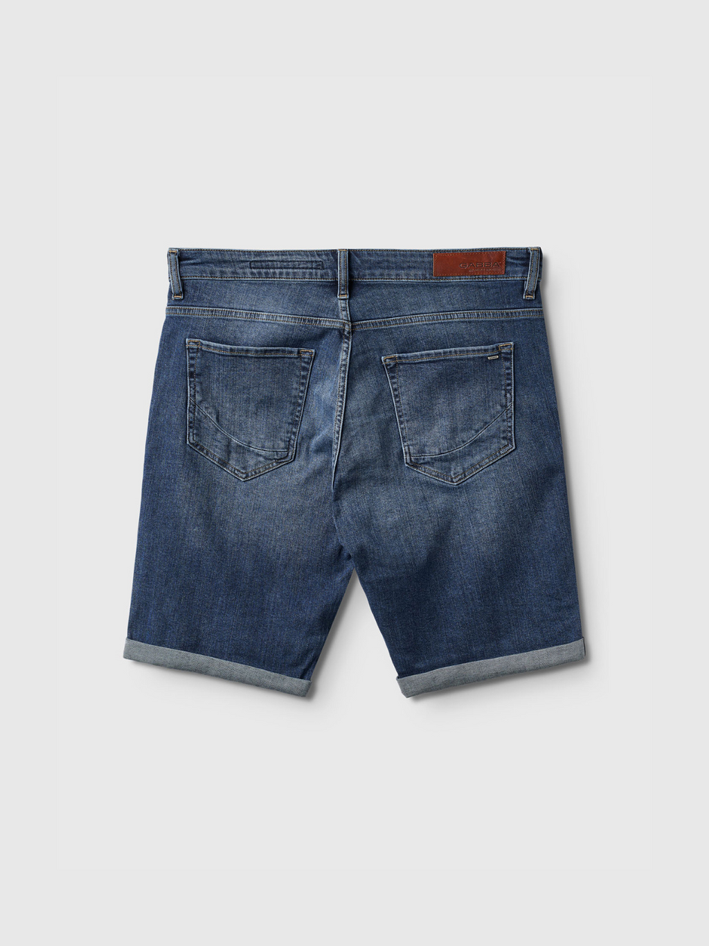 Back view of Gabba Markus K4664 Shorts in mid blue denim, featuring a comfortable fit, rolled hems, two back pockets, belt loops, and a brown leather patch on the waistband against a plain white background.
