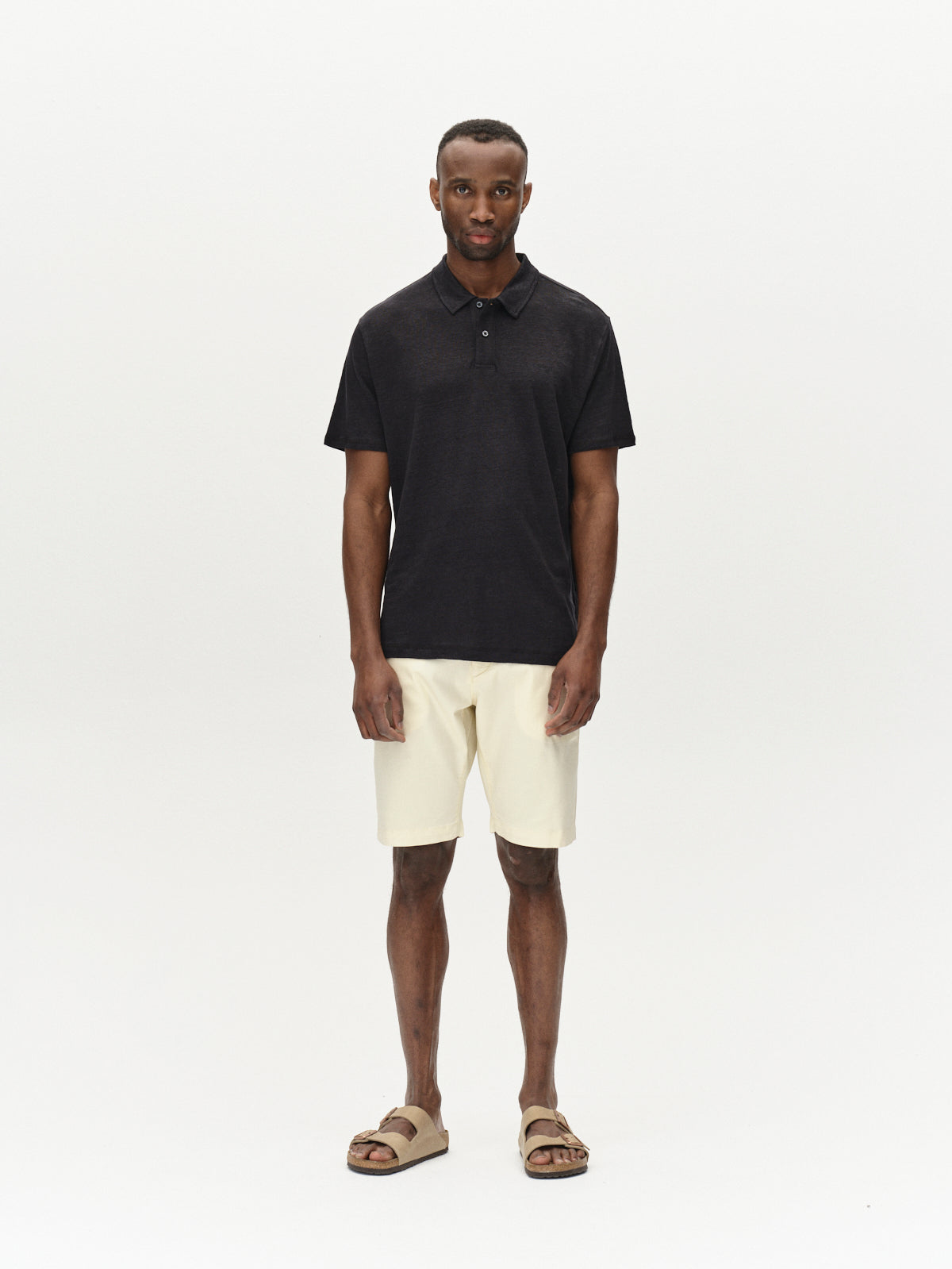 A person is shown against a plain background in a black polo shirt, Gabbas Jet K3280 Dale Shorts in Ecru Light, and brown sandals. They face the camera directly with arms at their sides, highlighting the outfits versatility.