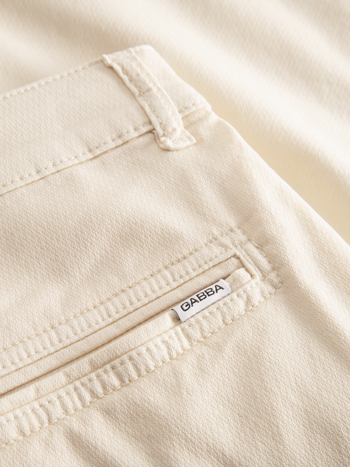 Close-up of ecru light shorts highlighting the back pockets versatile design. A small white label with Gabba is sewn above the seam. The fabric texture shows fine stitching and a neatly folded flap, part of the Jet K3280 Dale Shorts by Gabba.
