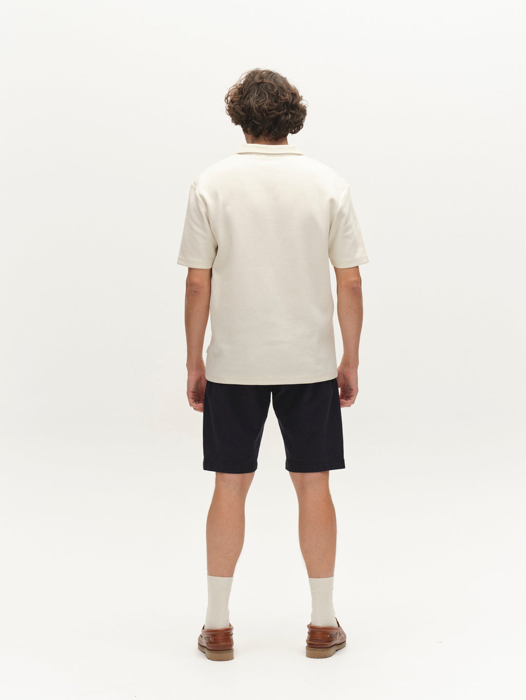 A person with short curly hair faces away, wearing Gabba’s GABjet K3280 Dale Shorts in Blue Black, a cream short-sleeve shirt, cream socks, and brown shoes against a white background—a timeless look for everyday wear.