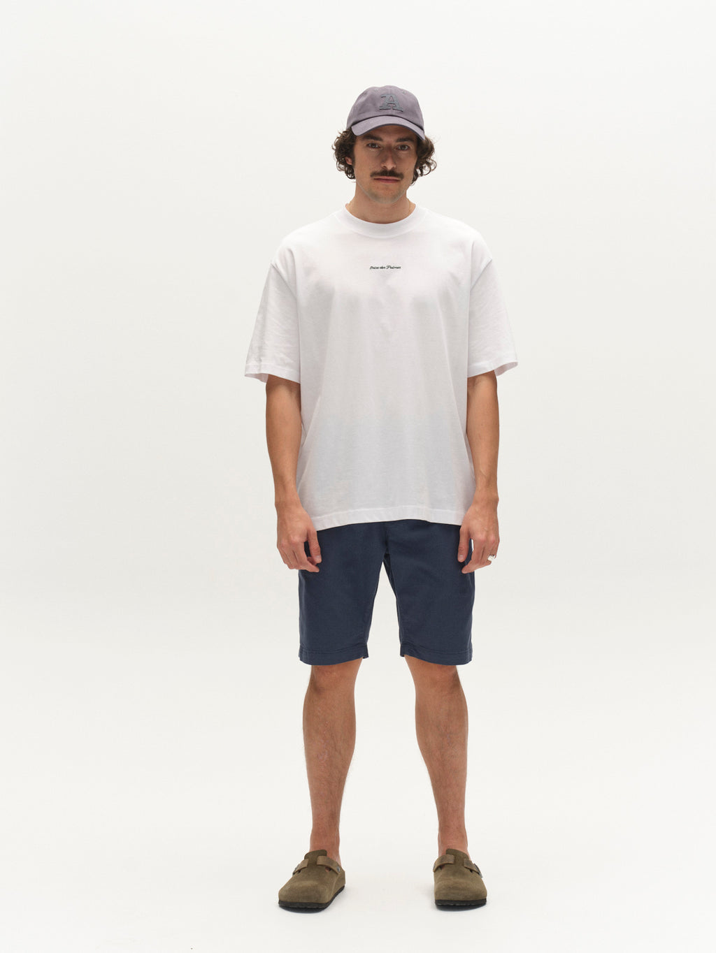 A man with a mustache and short curly hair wears a light purple cap, loose white t-shirt, Gabba GABjet K3280 Dale Shorts in Bering Sea, and brown slip-on shoes for an effortless everyday look against a plain white background.