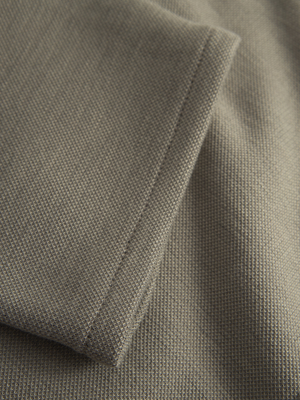 Close-up of a neatly stitched hem on light green structure fabric from Gabbas Paul GKnit pants, showcasing fine weaving and precise thread work.