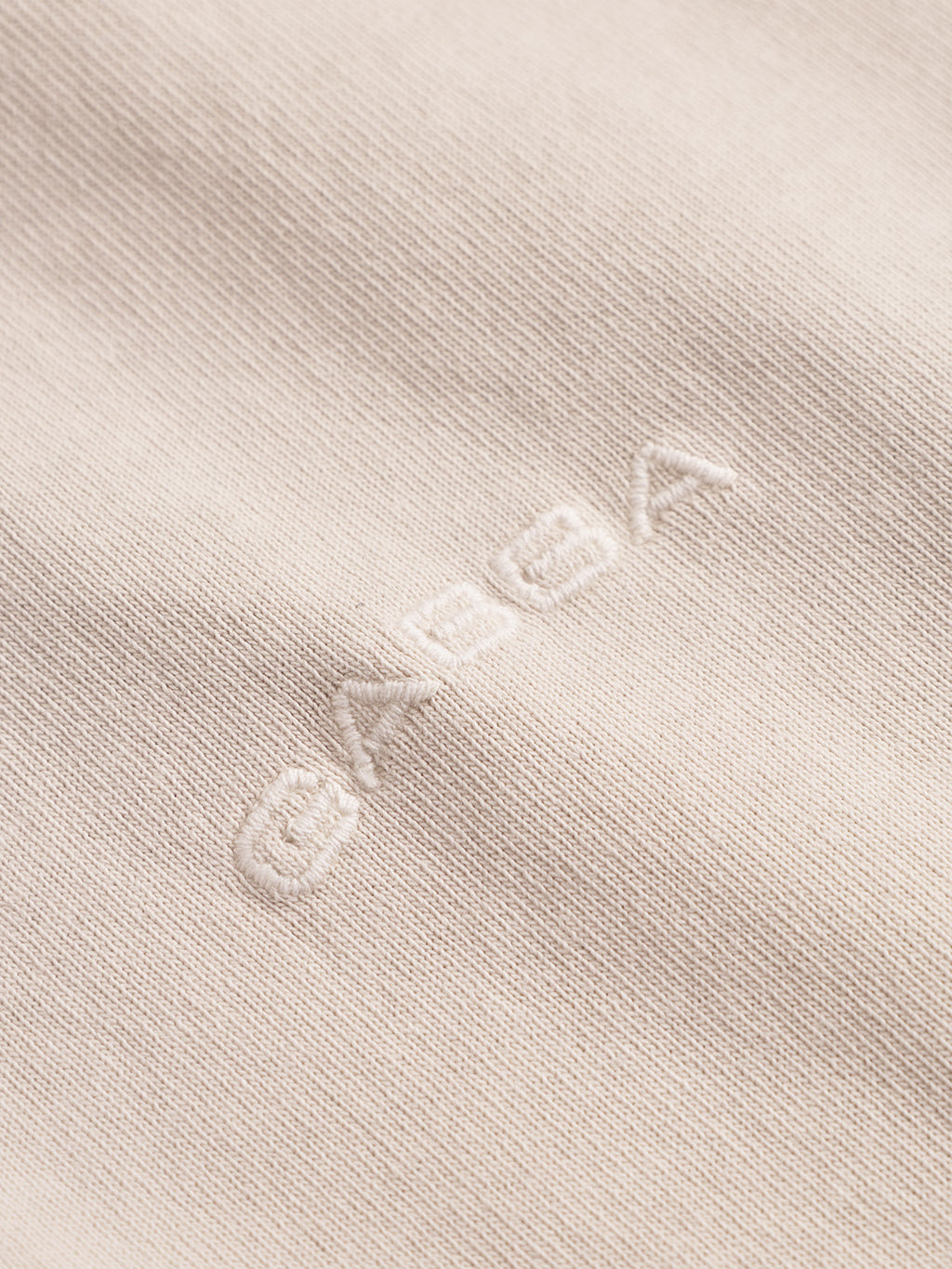 Close-up of garment-dyed cotton fabric from the Gabba Nigel Wix Boxy Hour SS - White Almond T-shirt, featuring “GABBA” embroidered in white thread. The detailed stitching and texture highlight its premium, boxy design.