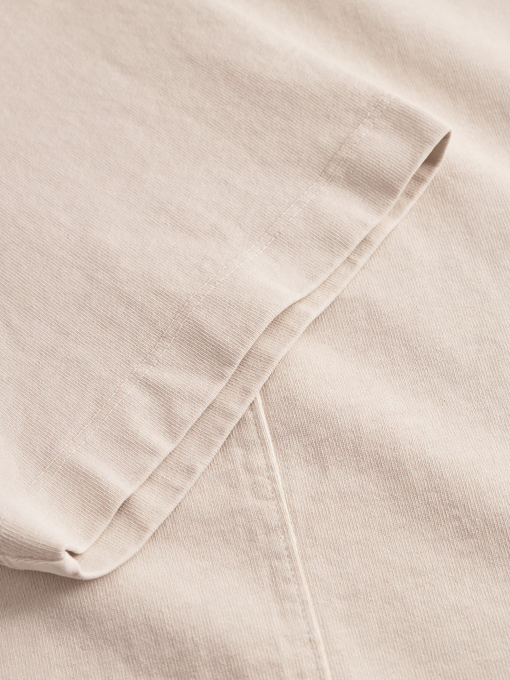 Close-up of Gabba’s Nigel Wix Boxy Hour SS - White Almond, focusing on the garment-dyed cotton fabric, folded edge with visible stitching, and textured weave typical of a boxy T-shirt.