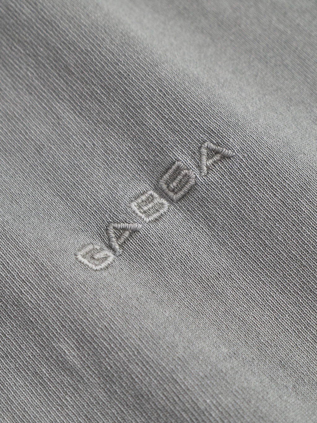 Close-up of Gabba’s Nigel Wix Boxy Hour SS in Dust Sage Green, featuring heavyweight cotton with “SABUK” embroidered in white, highlighting the vintage texture typical of boxy-fit t-shirts.