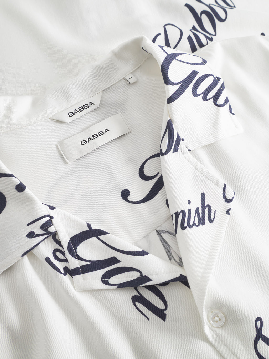A close-up of the Gabba Jens Over Resort Kiosk SS shirt in a navy pattern, made from 100% viscose. The collar is open with two Gabba tags visible, and the soft fabric is arranged for a comfortable look.