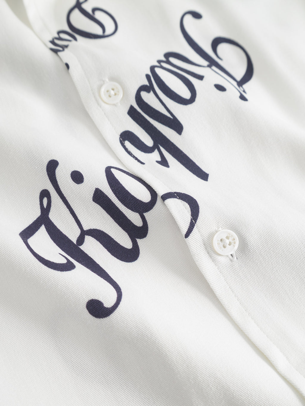 Close-up of the Gabba Jens Over Resort Kiosk SS shirt in Navy Pattern, crafted from 100% viscose. Features decorative black script text on the front, two visible white buttons, and a soft, smooth texture for comfort.