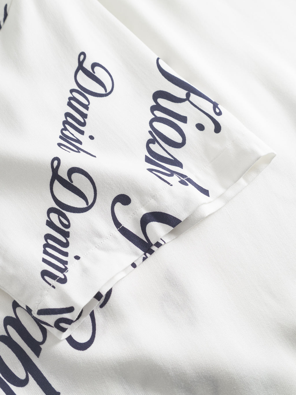 Close-up of the Gabba Jens Over Resort Kiosk SS in Navy Pattern, featuring white 100% viscose fabric with black cursive script and a visible sleeve, highlighting the premium shirts overlapping text details.