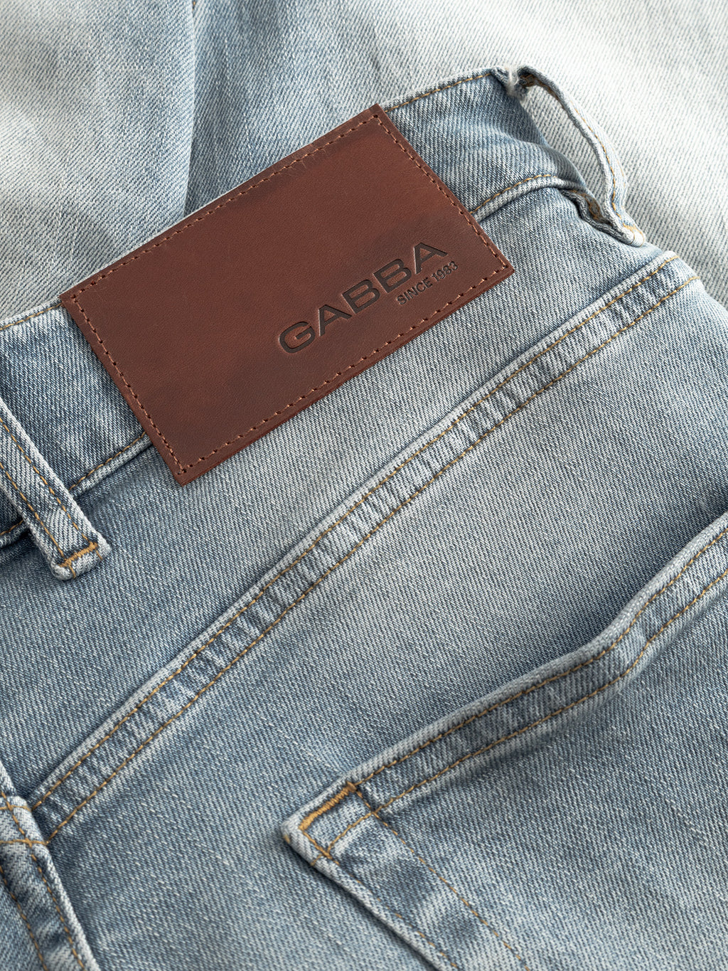 Close-up of GABalex Cros Cropped Lt. Blue Denim jeans by Gabba, made from recycled cotton, with a brown leather patch above the back pocket embossed with 
