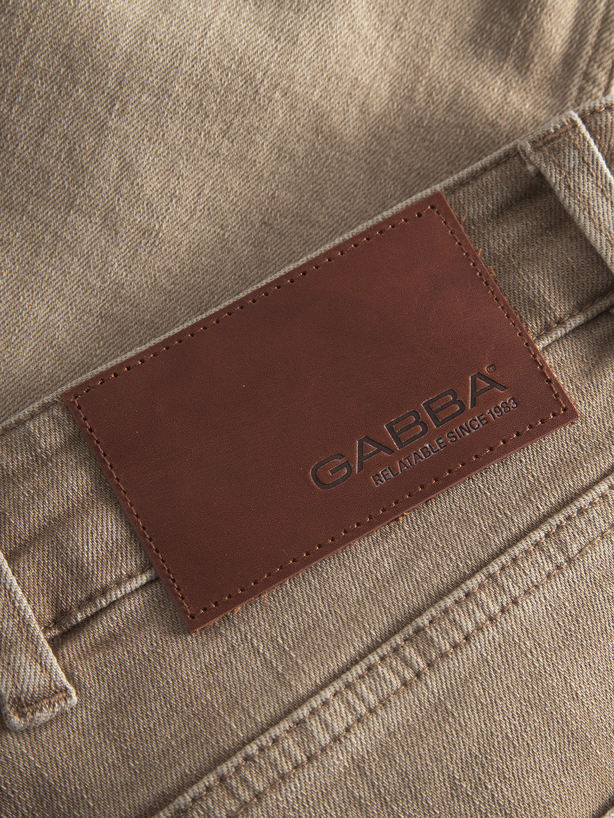 Close-up of a brown leather patch embossed with Gabba Reliable Since 1983, stitched onto the waistband of Alex Earth - Sand relaxed-fit beige denim jeans by Gabba.