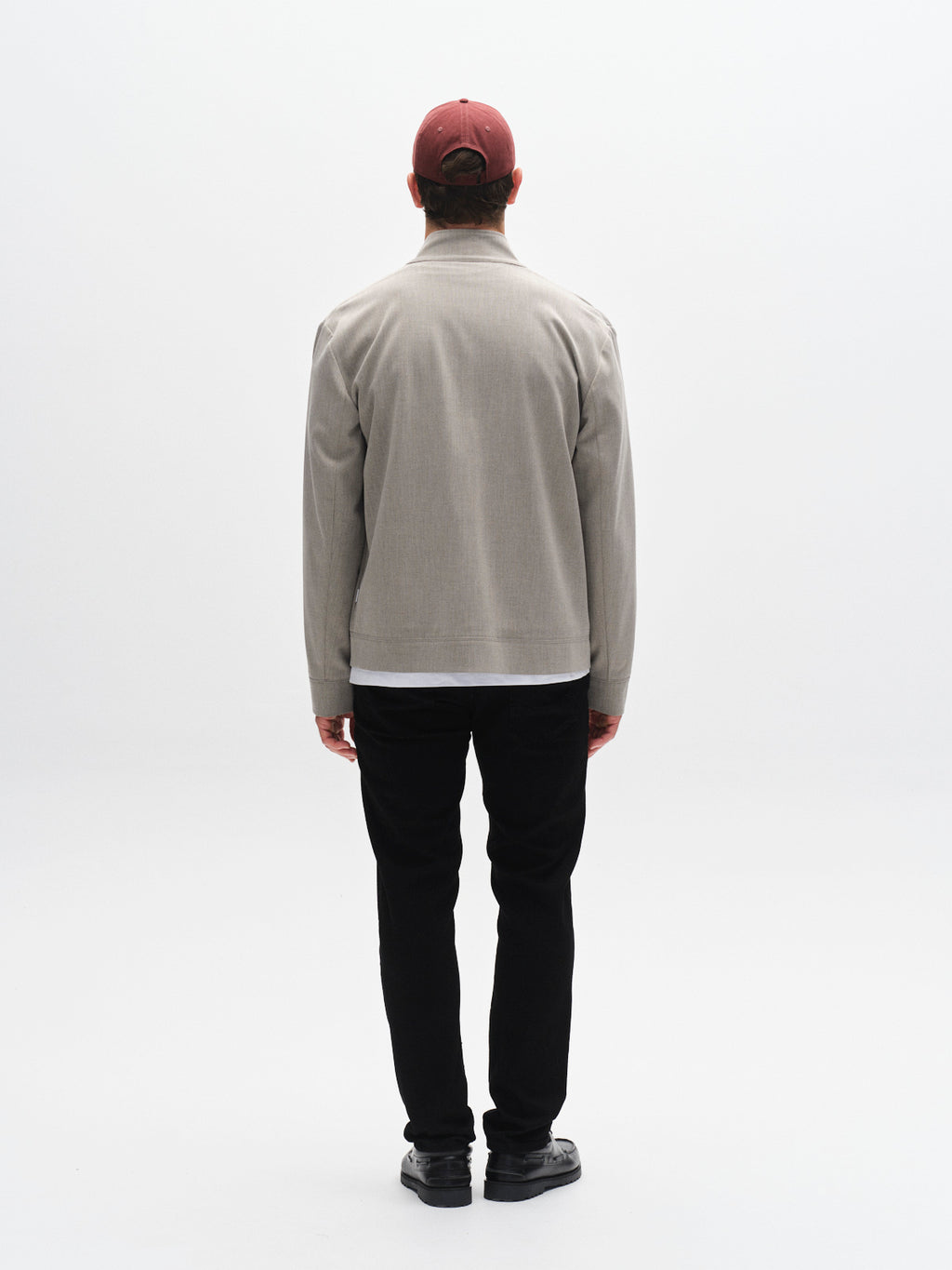 A man faces away from the camera, wearing a beige jacket, black shoes, a red baseball cap, and Gabba GABmarc Sword - Black Denim modern slim fit pants against a plain white background.