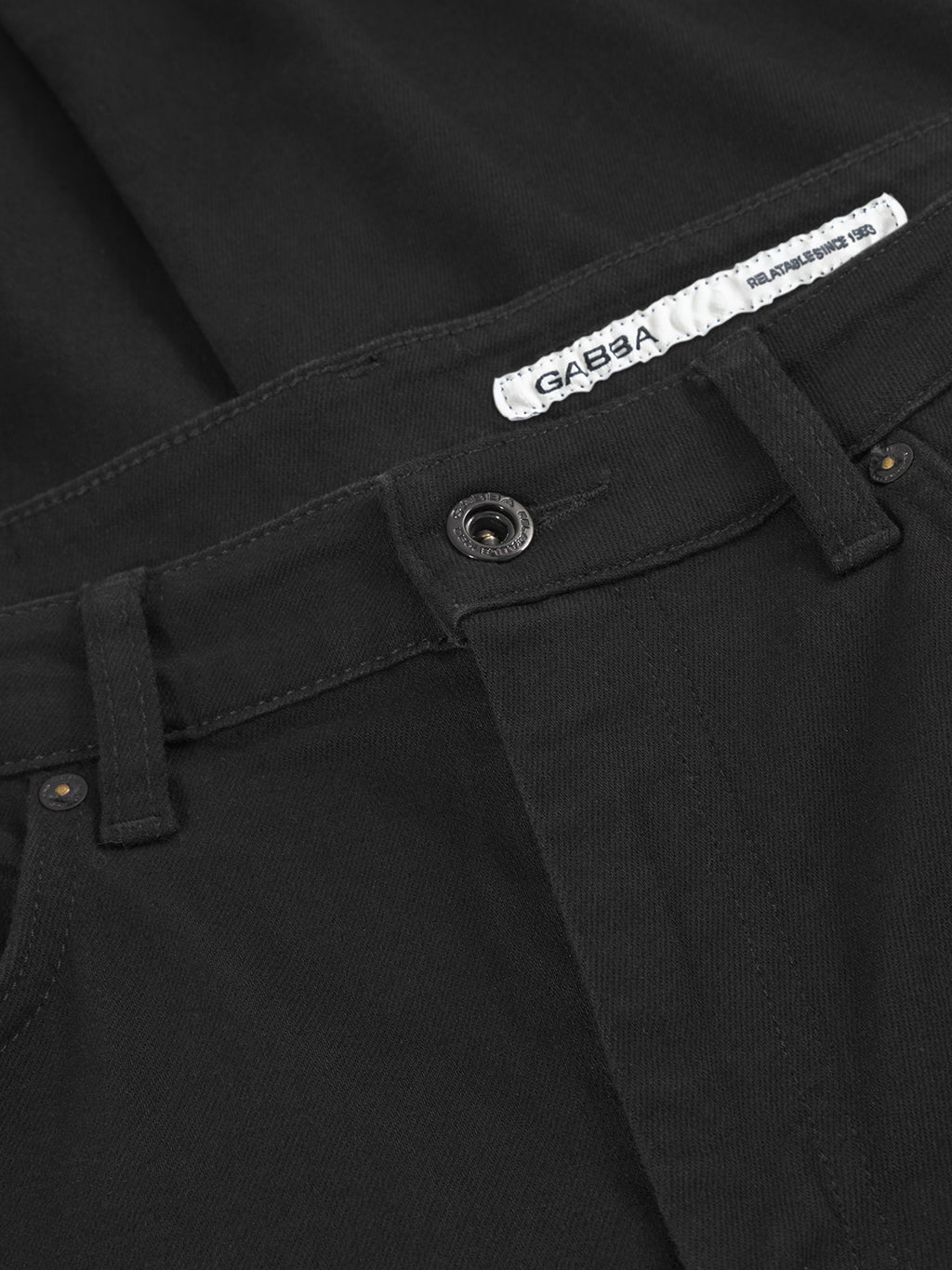 Close-up of the waistband and button of GABmarc Sword - Black Denim jeans by Gabba, partially open to reveal a white Gabba label inside. The deep black slim-fit denim shows off its texture and detailed stitching.