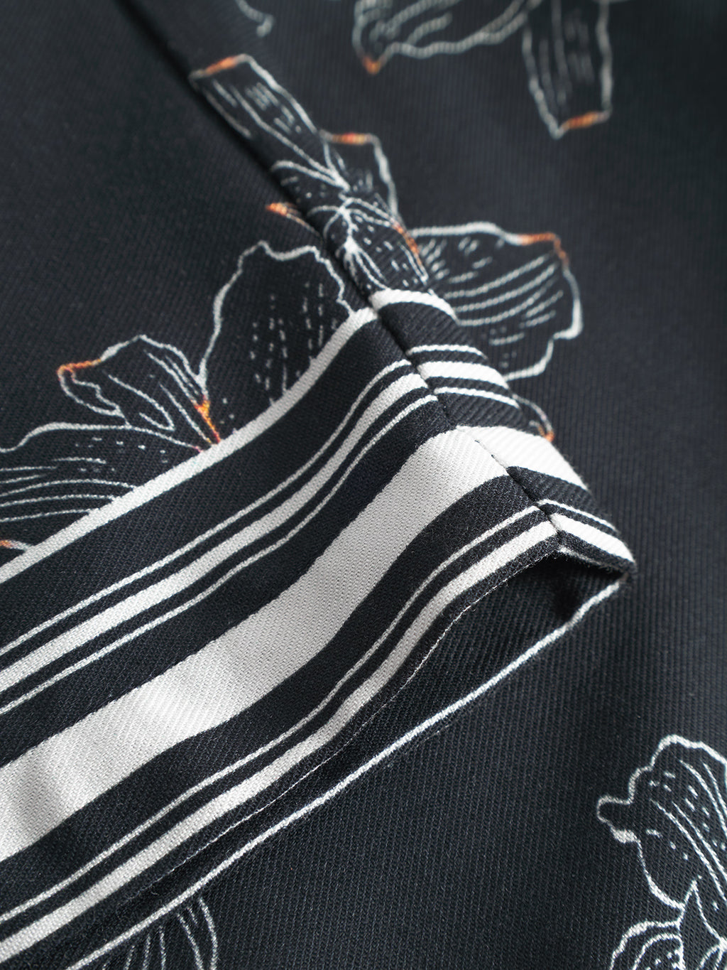 Close-up of Gabba Porter Lofi - Flower Mix shorts showing black fabric with white floral patterns, diagonal striped trim, an elastic waistband, and visible stitching and texture.