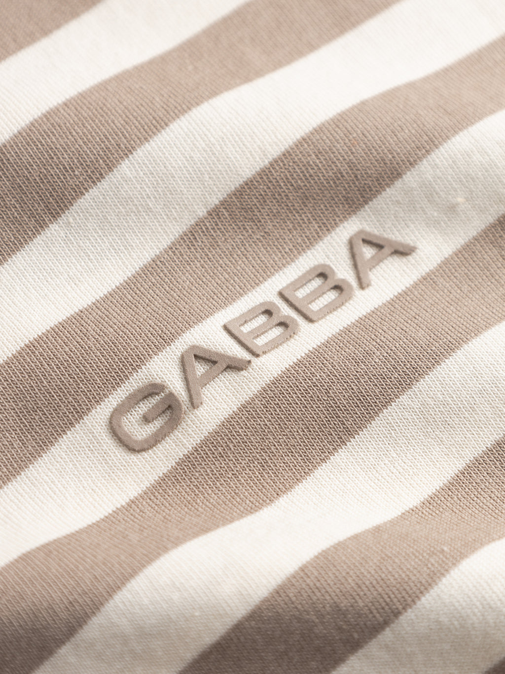 Close-up of Gabba’s GABdune Logo Stripes SS GOTS - Fungi t-shirt fabric in beige and white stripes, featuring raised GABBA lettering—a stylish detail for this classic, GOTS-certified tee.