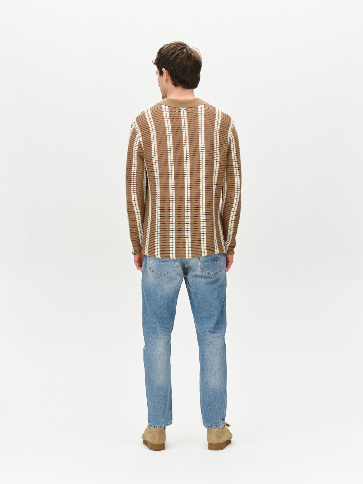 With their back to the camera, a person embraces a stylish casual look in a brown sweater with white stripes. They wear Gabbas Carl Astra Mid Blue Denim, which features a loose tapered fit, perfectly paired with tan shoes against a plain white background.