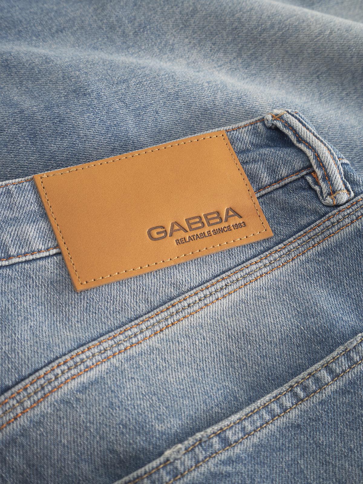 Close-up of Carl Astra - Mid Blue Denim jeans with a leather patch reading GABBA RELIABLE SINCE 1983 stitched on the waistband above a pocket, highlighting the Gabba brands logo and craftsmanship. These jeans offer comfort and style with their loose tapered fit.