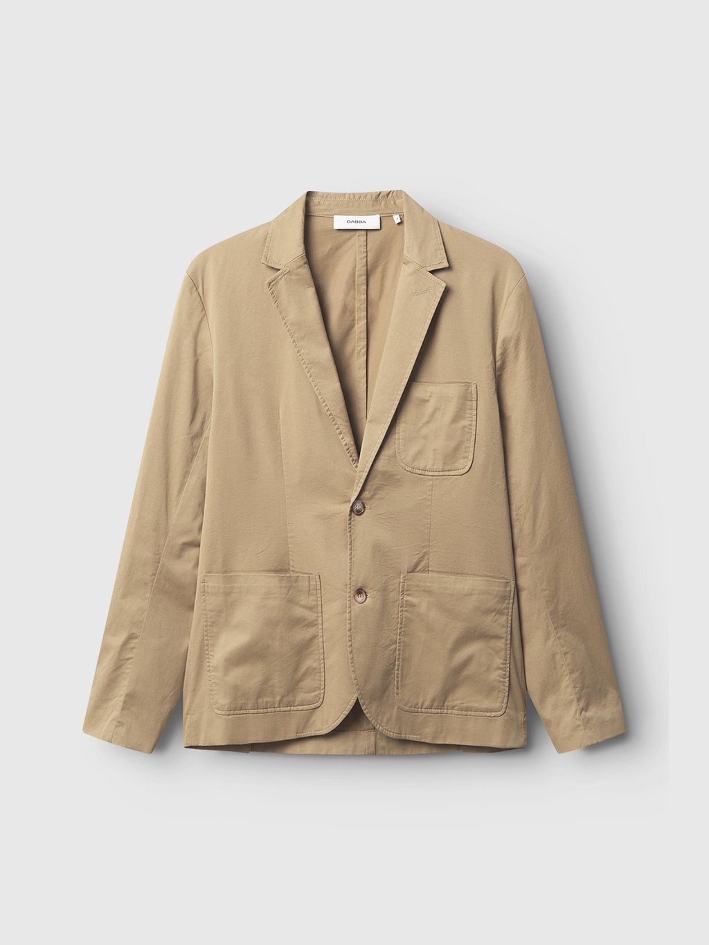 The Gabba Josh Unite - Sand is a premium beige cotton stretch blazer with three front patch pockets, two buttons, and a notched collar, shown on a plain white background.