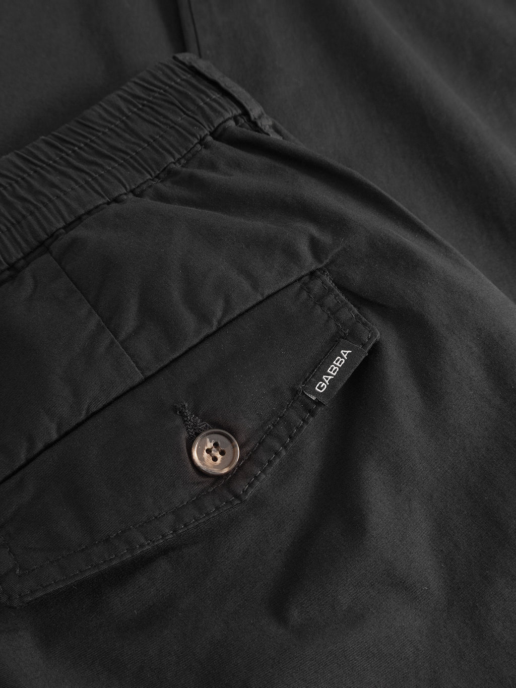 Close-up of the Gabba Monza Unite - Black pants showing a pocket with a brown button, stitched flap, and small black GABBA tag. The elastic waist adds comfort to this classic silhouette.