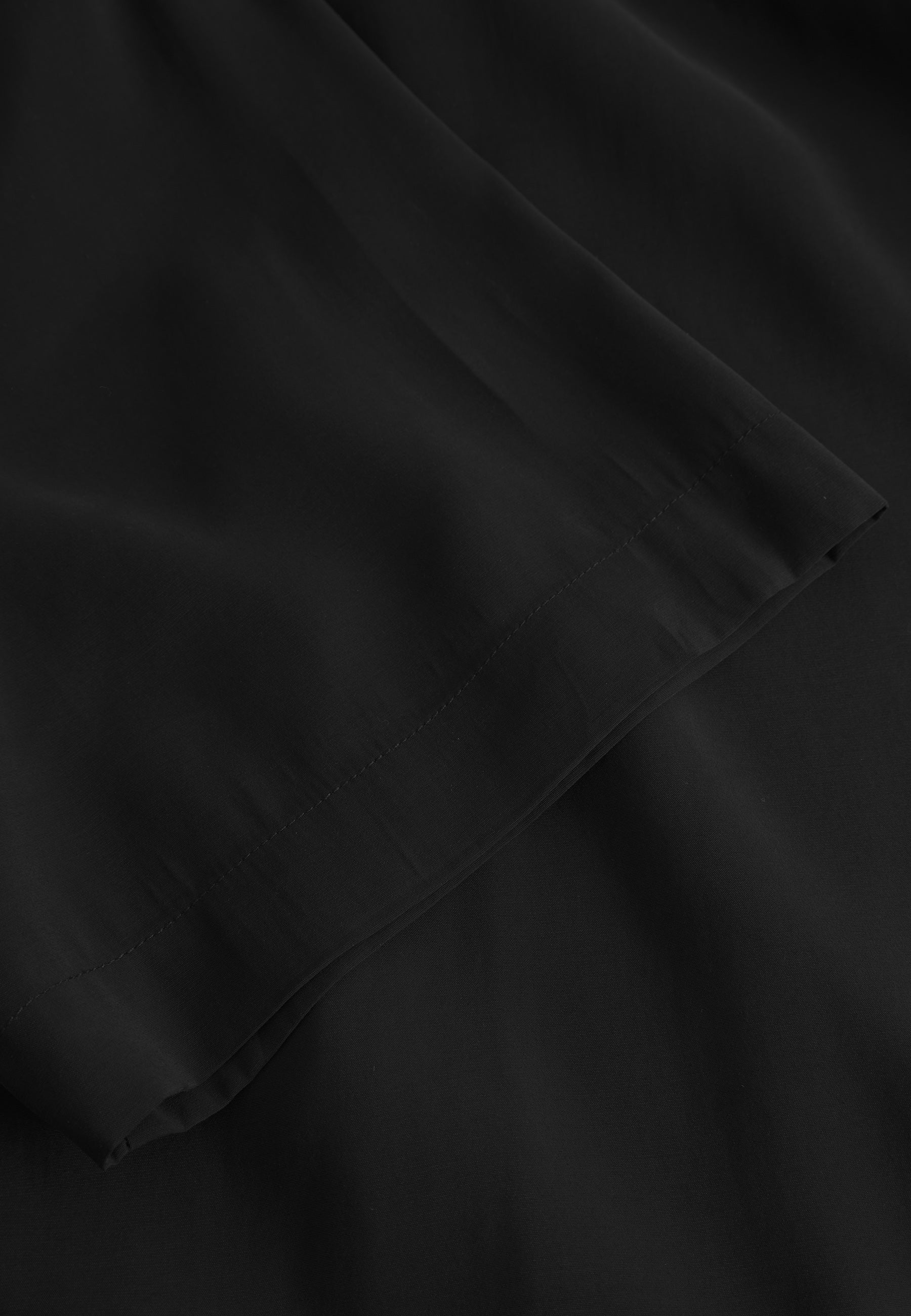 Close-up of the Jens Over Resort Yari SS - Meteorite by Gabba, showcasing a black fabric with a smooth texture. The edge is neatly stitched, and the material drapes naturally with a soft, slightly shiny finish, evoking premium shirt craftsmanship.