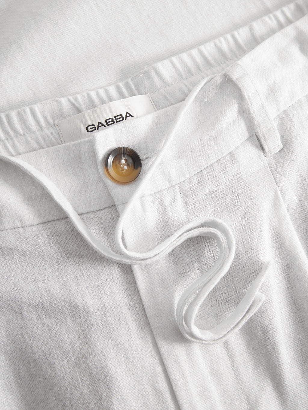 Close-up of Gabba’s Napoli 19 Side Lino - White pant featuring a brown button, white drawstring, and signature label. The soft, textured fabric offers relaxed style and comfort.