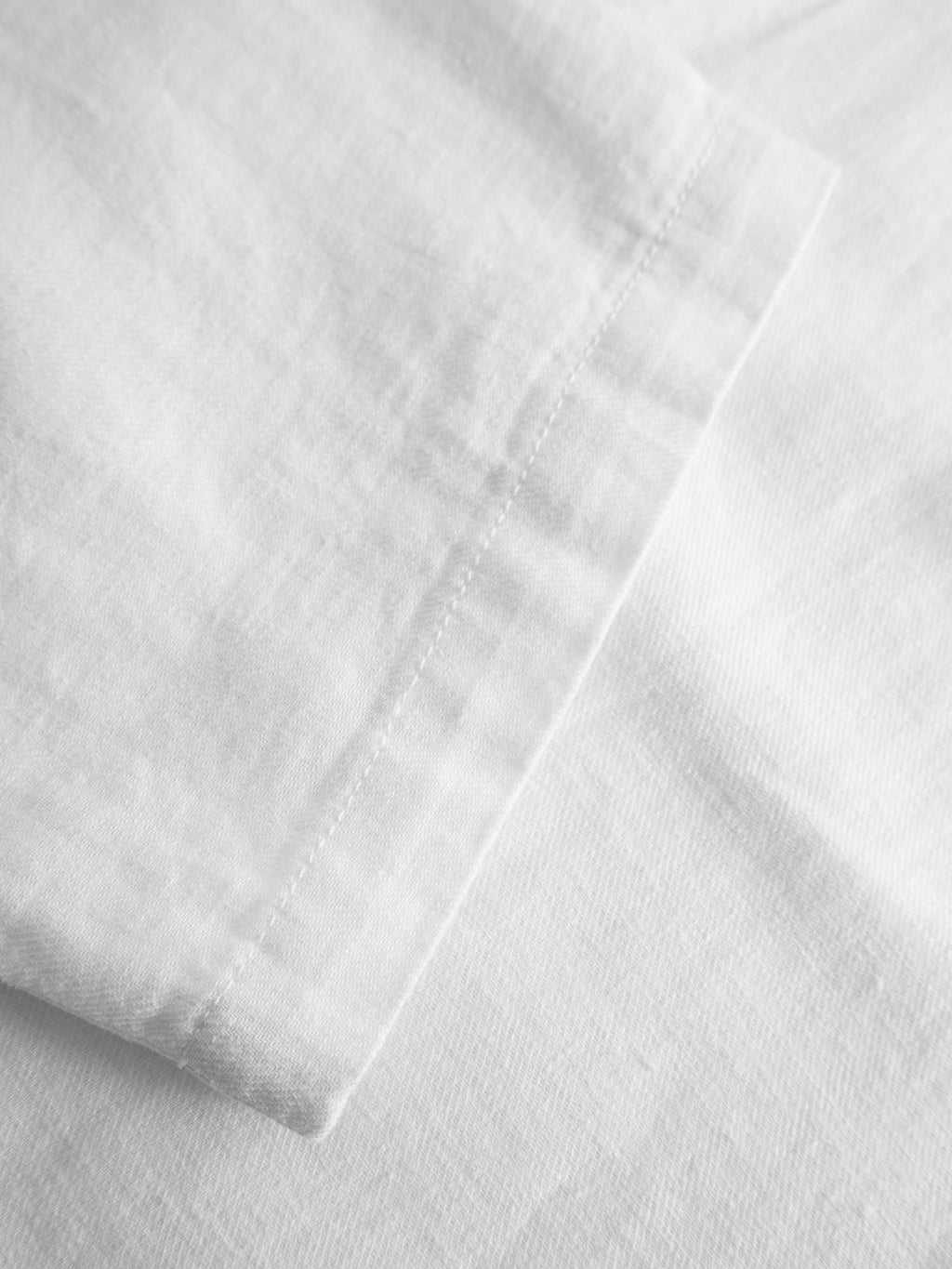 Close-up of the white fabric and hem stitching detail of the Napoli 19 Side Lino - White pant by Gabba, showcasing its relaxed vibe, style, and comfort against a matching background.