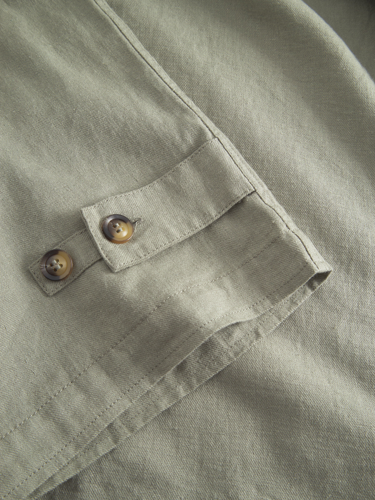 Close-up of Peter Lino - Light Green by Gabba, featuring textured beige linen/cotton fabric with brown buttons on a flap. This piece is a perfect spring companion offering gentle textures and subtle warmth, suggesting it’s part of a light overshirt.