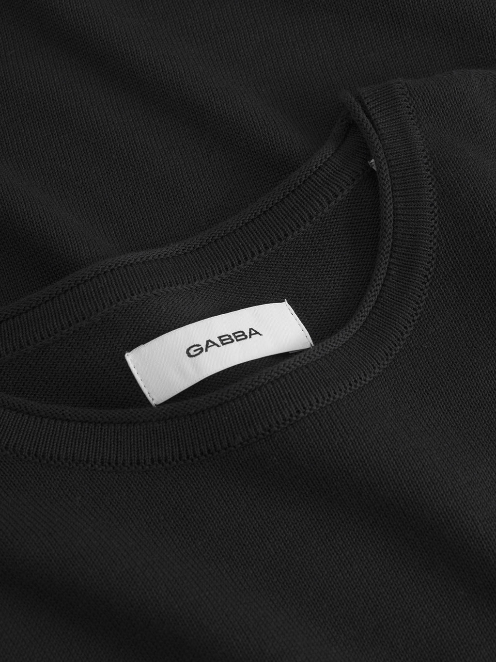 Close-up of the Gabba Bela Fix LS - Meteorite, a black cotton crew neck shirt featuring a white inner collar label with “Gabba” in black text. The detailed knit construction and stitching promise lasting comfort.