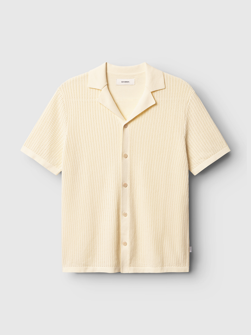 The Gabba Geno Resort SS - Ecru Light, a short-sleeved shirt with a textured woven pattern, relaxed fit, button-down front, and spread collar, is showcased against a light gray background.
