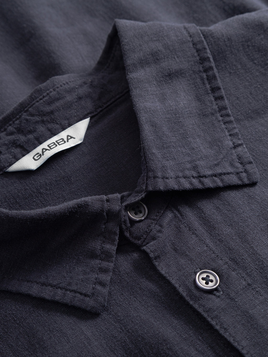 Close-up of the Gabba Sven Reg Lino SS - Night Sky, a premium dark navy button-up shirt featuring garment-dyed, textured fabric, two dark buttons, and a visible white collar label with the Gabba brand.
