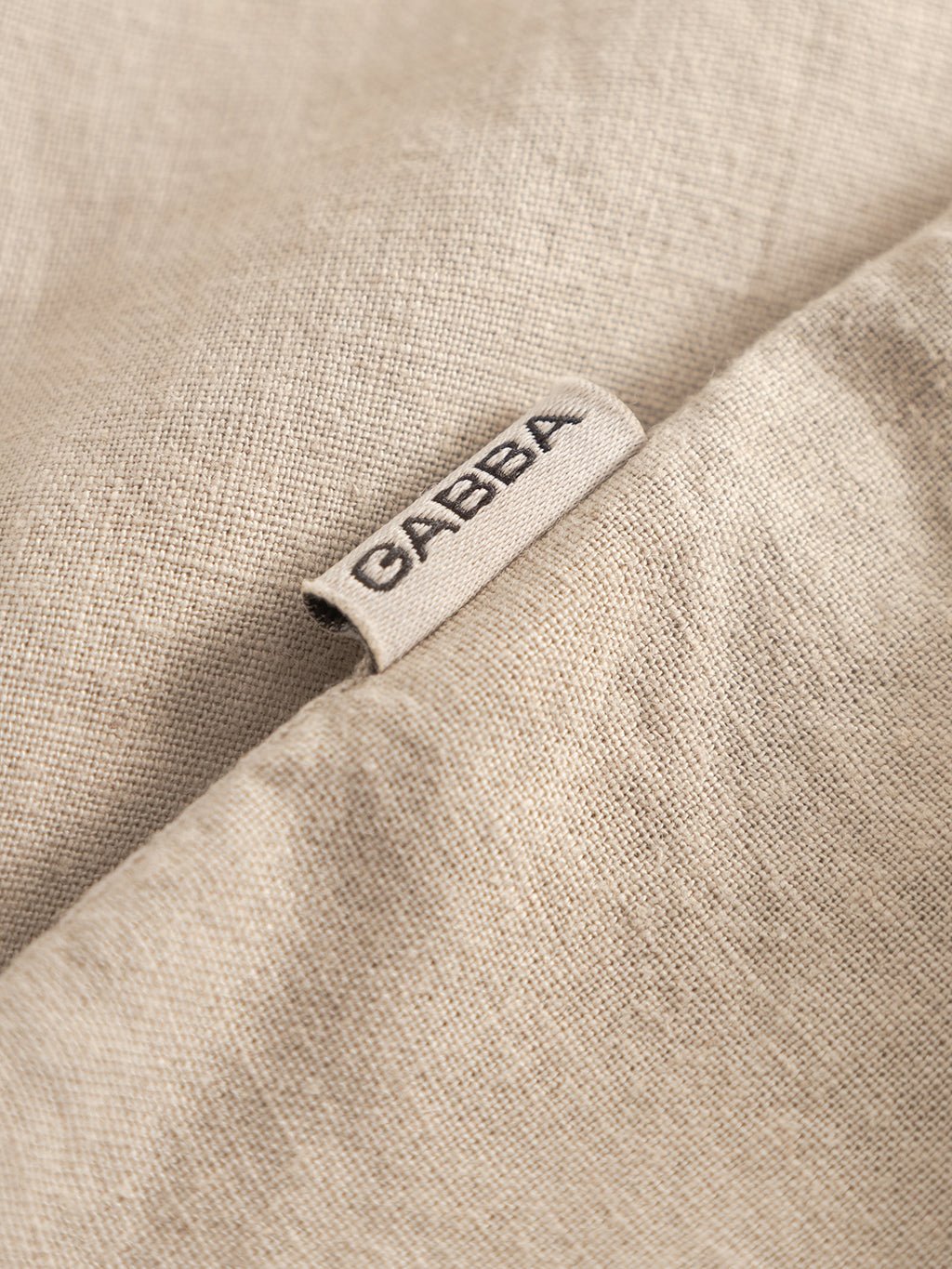 Close-up of the Sven Reg Lino LS - Sand Plaza by Gabba, featuring beige garment-dyed linen with a small Gabba tag stitched into the seam—ideal for a premium shirt.