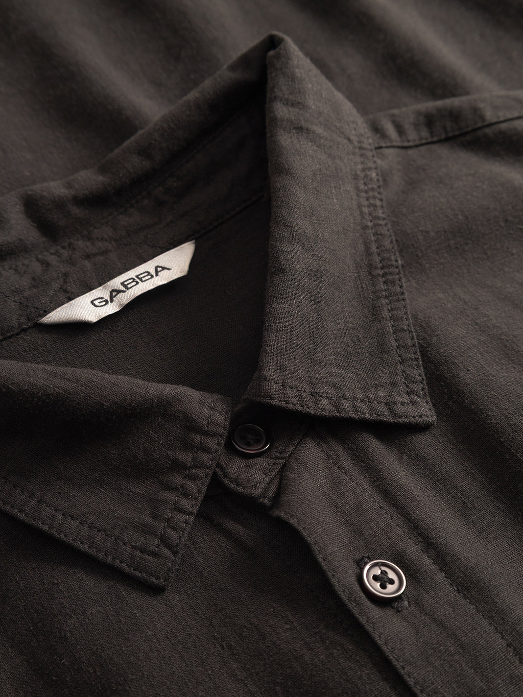 Close-up of a black Gabba Sven Reg Lino LS - Meteorite premium shirt with buttons and a visible white label featuring the brand name.