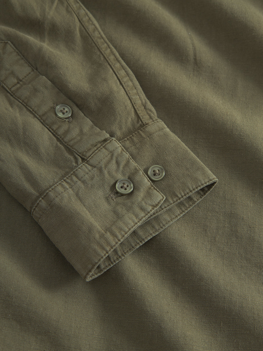 Close-up of Gabbas Sven Reg Lino Mand LS - Olive Green shirt cuff, showing two buttons, fine stitching, and the textured linen-blend fabric. The long-sleeve shirt is displayed flat.