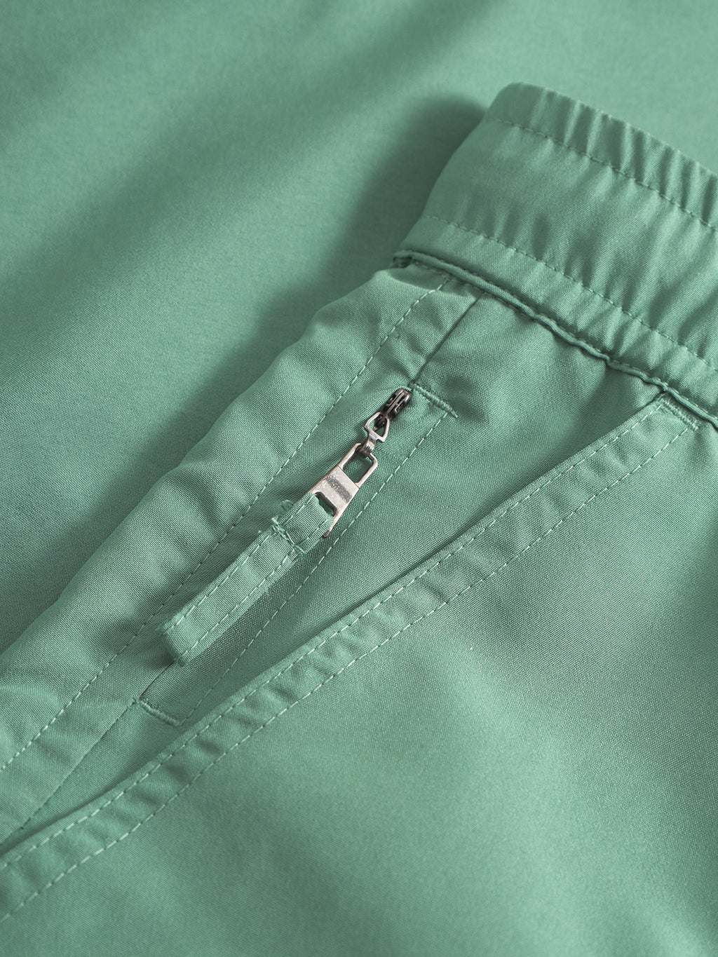 Close-up of Gabbas Jackson Plain - Green Sea swim shorts, featuring an elastic waistband, neat stitching, and a zippered side pocket.