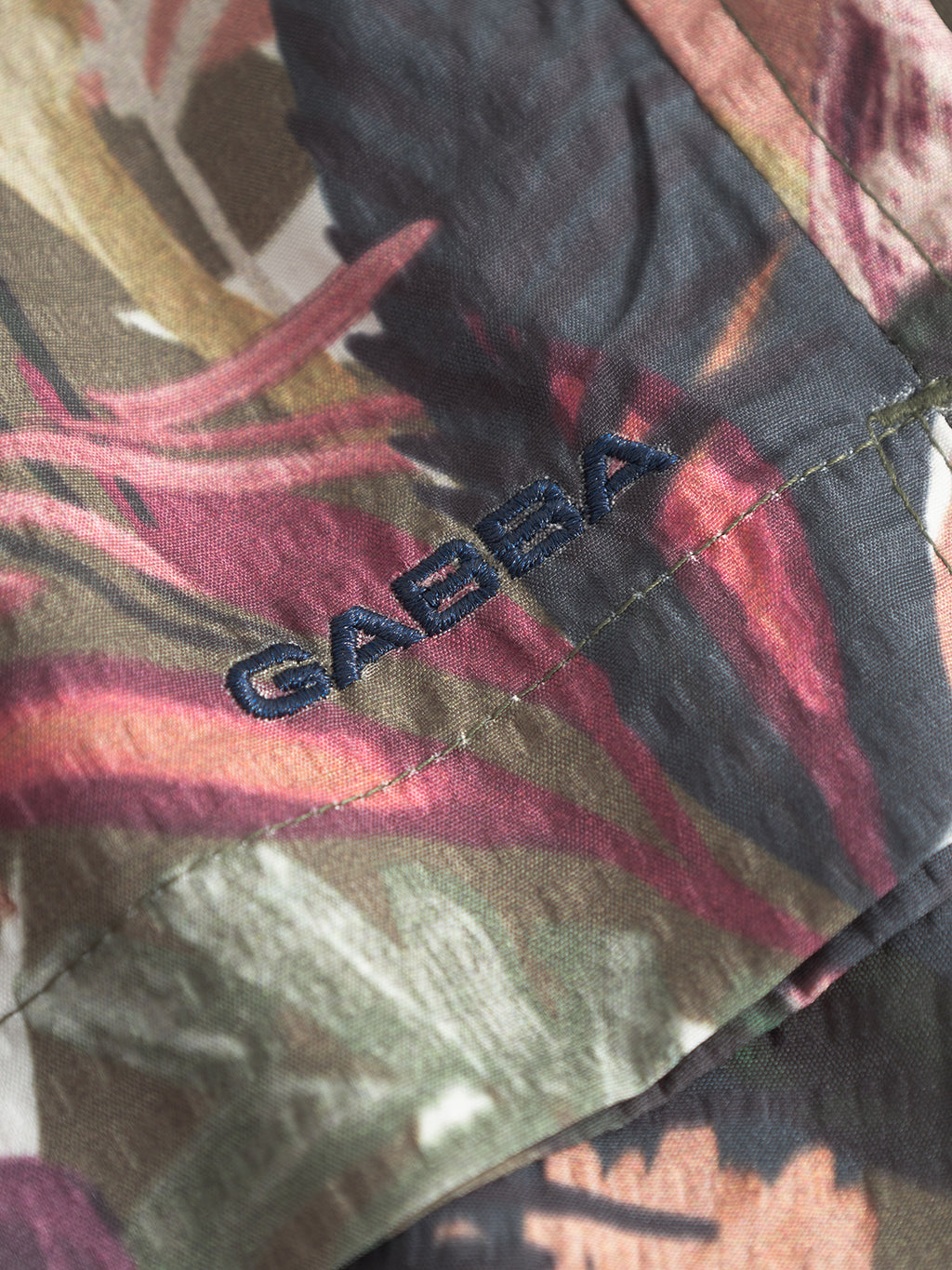 Close-up of Gabba Jackson Seer Print - Flower Mix swim shorts fabric, featuring a colorful tropical leaf pattern, elastic waistband, side pockets, and GABBA embroidered in dark blue thread.