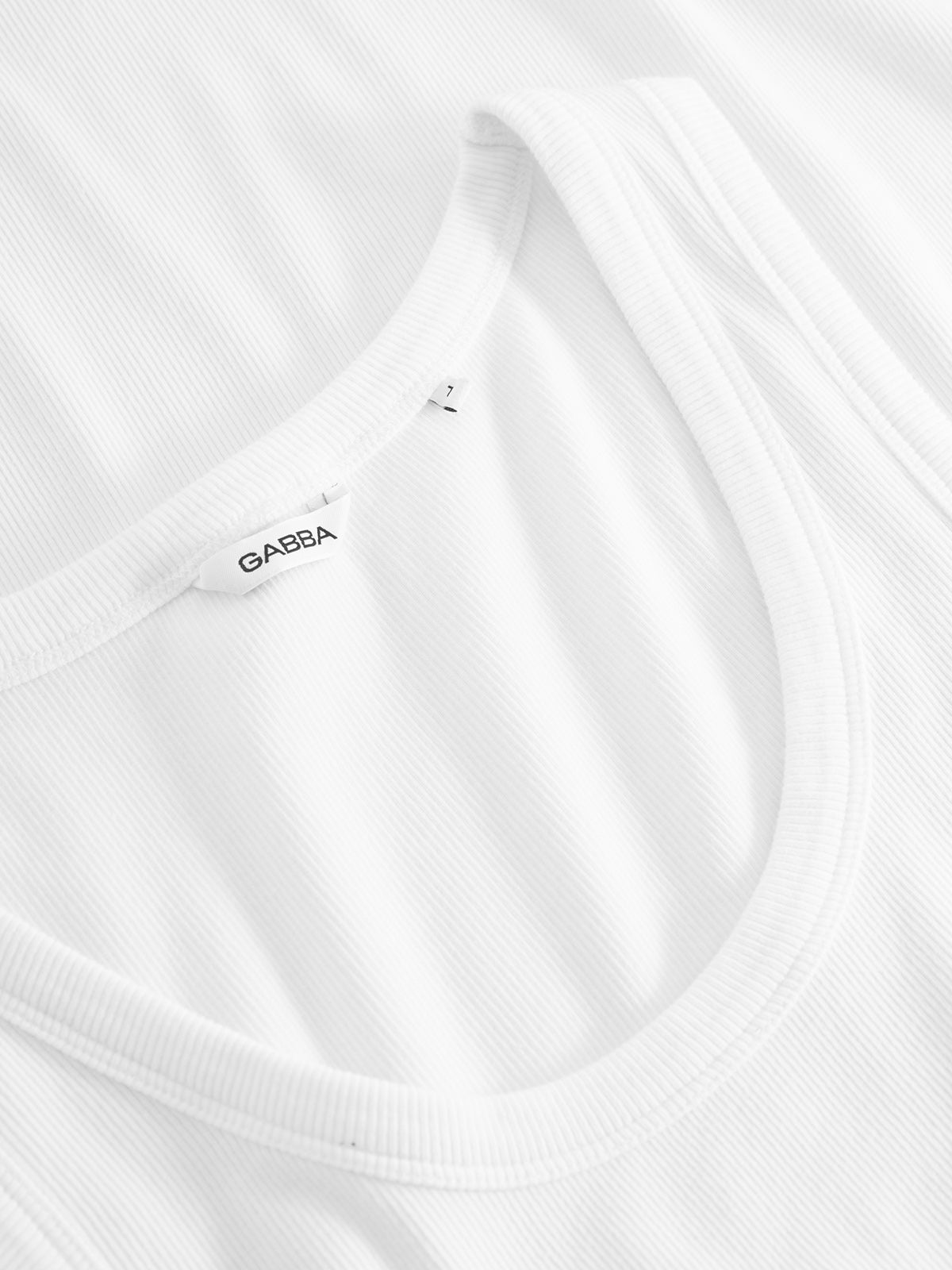 A close-up of the Orsen - White cotton ribbed tank top shows its soft texture. It is laid flat with a small Gabba label near the collar, making it perfect for summer days.