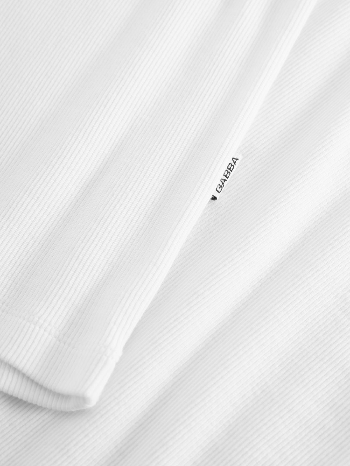 Close-up of Orsen - White by Gabba, featuring a white textured cotton fabric with ribbed lines. The small tag displays text in black, evoking breezy comfort perfect for warm summer days.