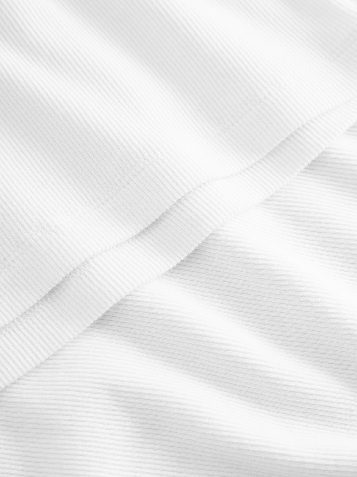 Close-up of Gabbas Orsen - White fabric, with two layers of ribbed cotton visible. The light highlights the texture and folds, reminiscent of a breezy summer tank top, emphasizing the materials intricate weave detailing.
