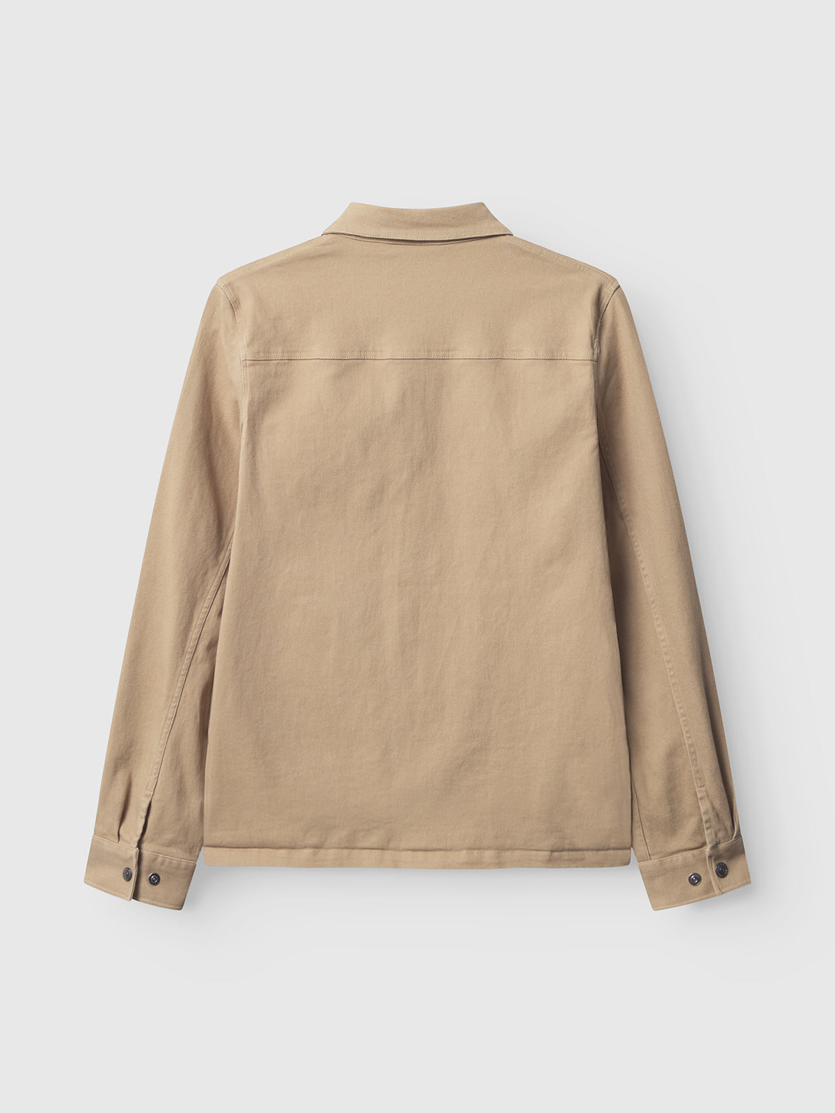 The Gabba Beta Twill - Sand overshirt is seen from the back, showcasing buttoned cuffs and a straight hem. Crafted from garment-dyed twill, it appears against a plain white background.