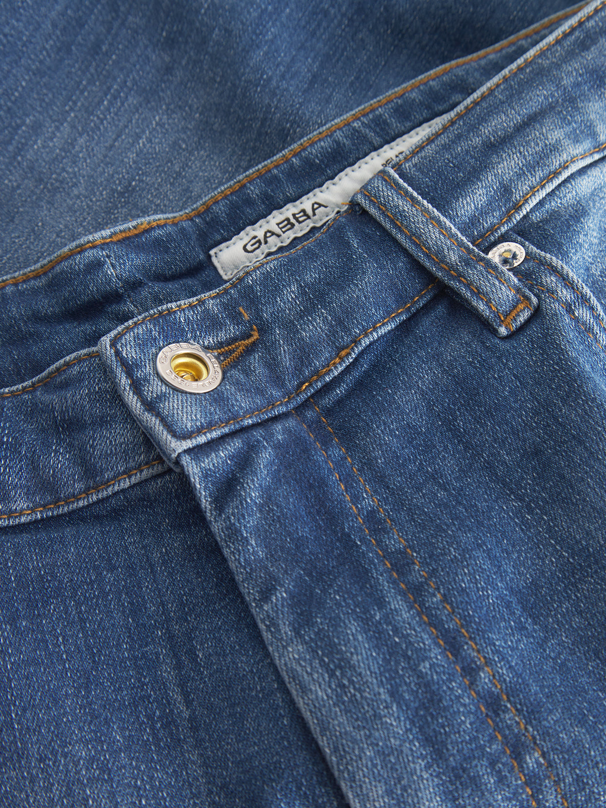 Close-up of Gabbas Markus Selvedge Shorts in Mid Blue Denim, showcasing visible stitching, a metallic button, and a white label. Comfortable fit is enhanced by slight color variations and soft texture, highlighting the weave. Crafted with recycled viscose for an eco-friendly touch.