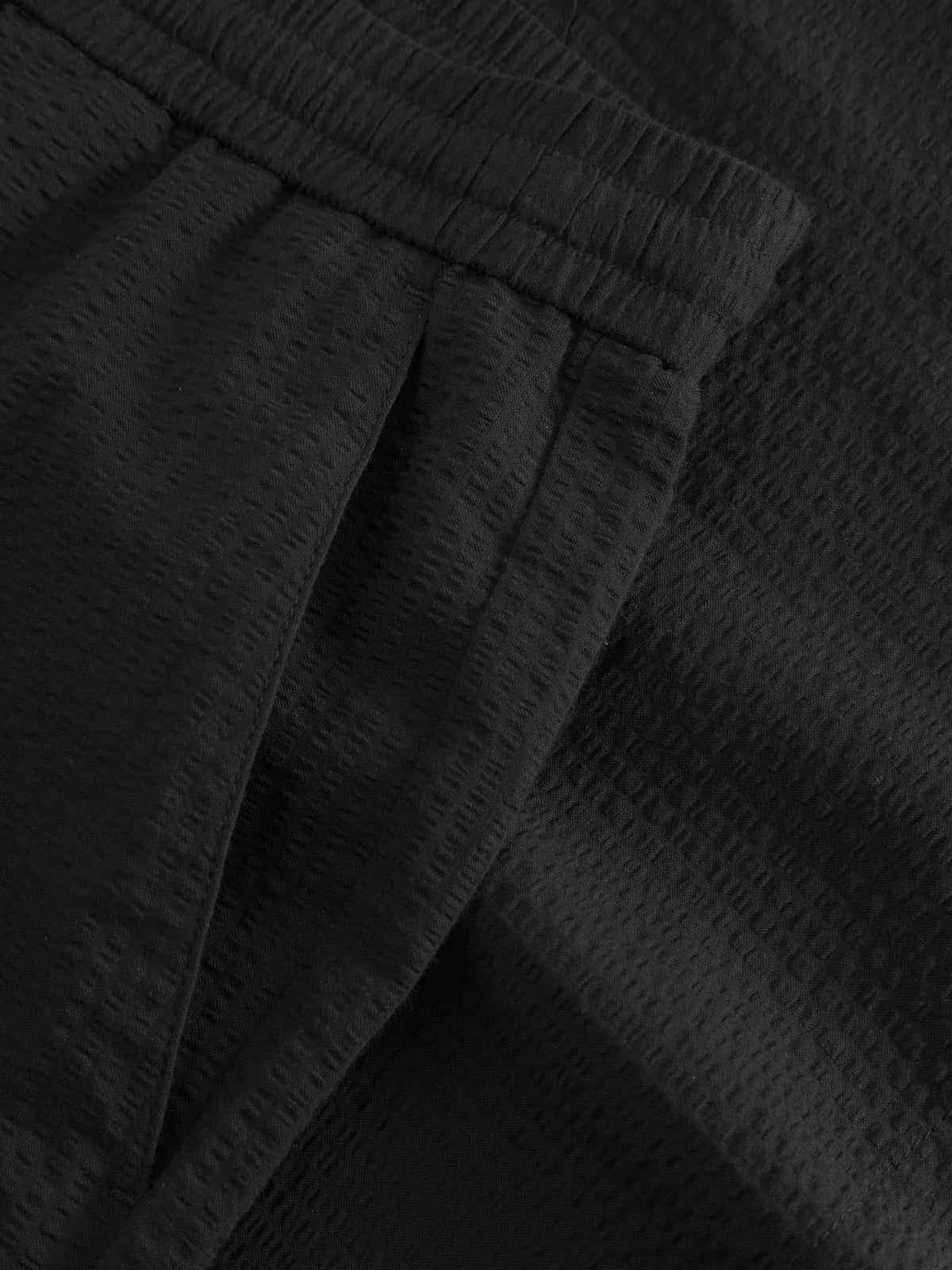 Close-up of black seersucker fabric showcases the waistband and side seam of Gabbas Tommi Seer premium shorts, highlighting the textured crinkle pattern and detailed 100% cotton stitching.