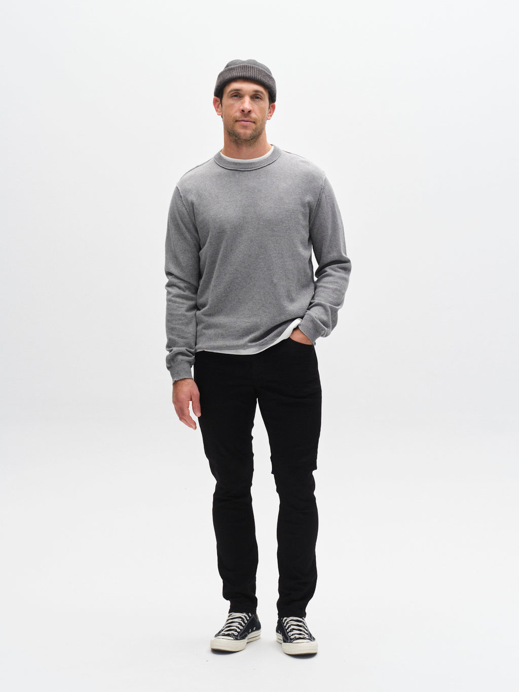 A man wearing a grey beanie, grey sweatshirt, and Gabba GABjones Hold Black - Black Denim slim-fit super-stretch jeans stands against a plain white background with one hand in his pocket.