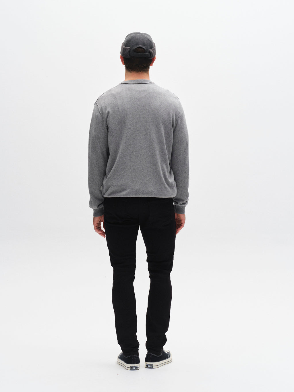 A person stands facing away from the camera, wearing a gray long-sleeve shirt, black cap, black-and-white shoes, and Gabba GABjones Hold Black - Black Denim slim silhouette jeans with super-stretch fabric, against a plain white background.