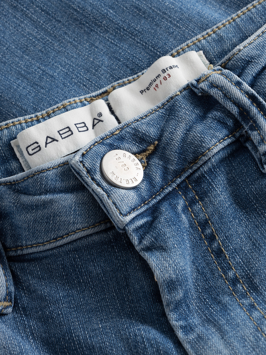 Close-up of GABBA GABjones K2615 Lt. denim wash jeans showing the waistband, metallic GABBA-engraved button, and branded inner label with size details. Made from super-stretch fabric for high flexibility.
